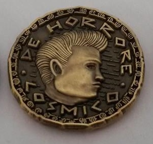 Bronzed coin of a man's face in profile, with the lettering "De Horrore Cosmico."