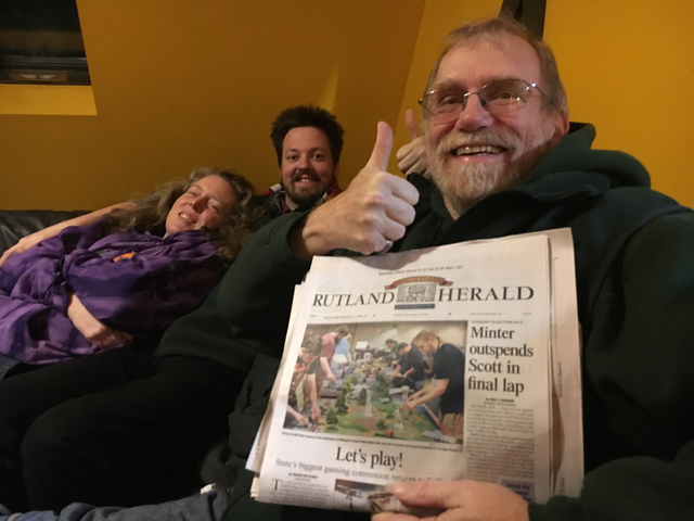 An older man with glasses and a beard gives a thumb's up while holding up a newspaper with a front page article about Carnage, with the headline 'Let's play!'