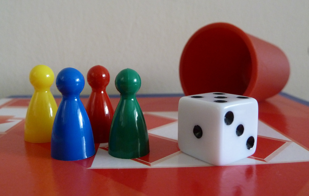 Traditional game pieces: four colored pawns, a six-sided die and a red cup for rolling dice.